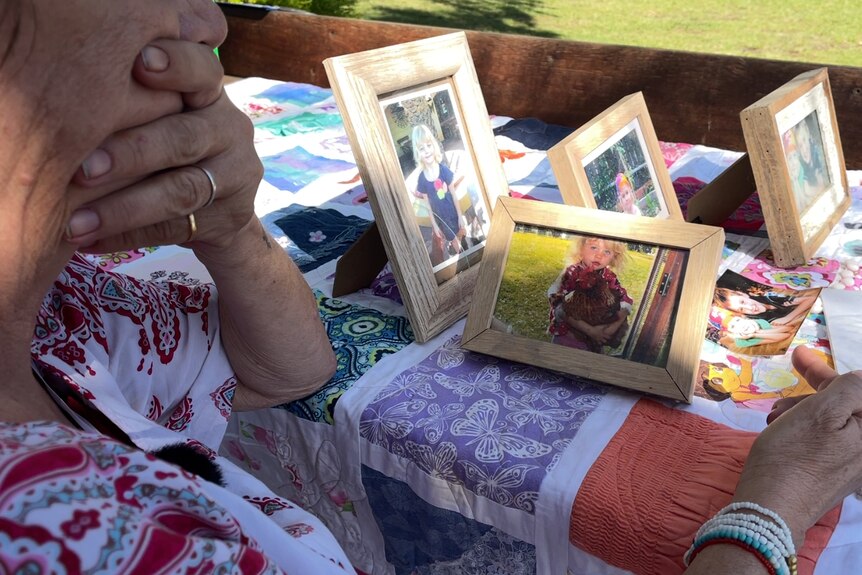 A woman holds her chin in her hand as she looks at framed photogarphs of a little girl.
