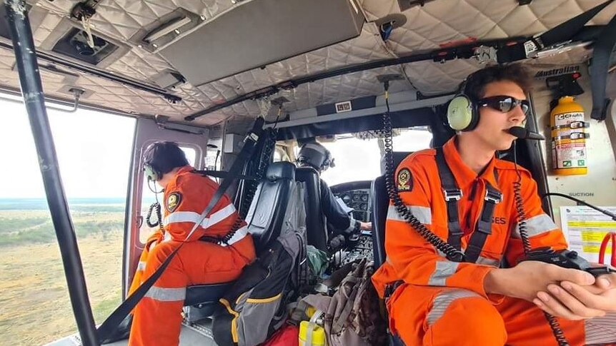 Two SES crews sit in a helicopter flying over remote bushland