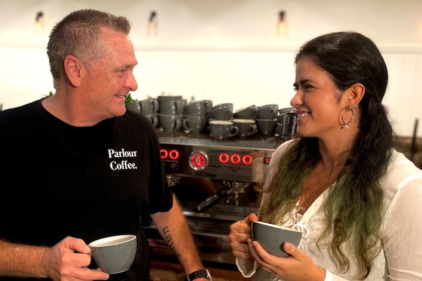 A middle-aged man stands next to a younger woman who is holding a coffee.