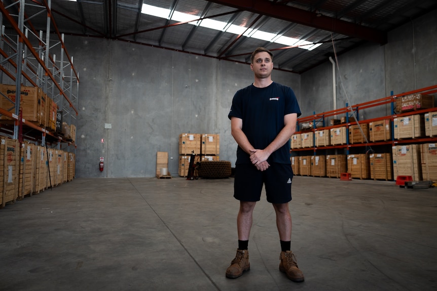 Jordan stands in a sparse, concrete warehouse, with a few shelving racks.