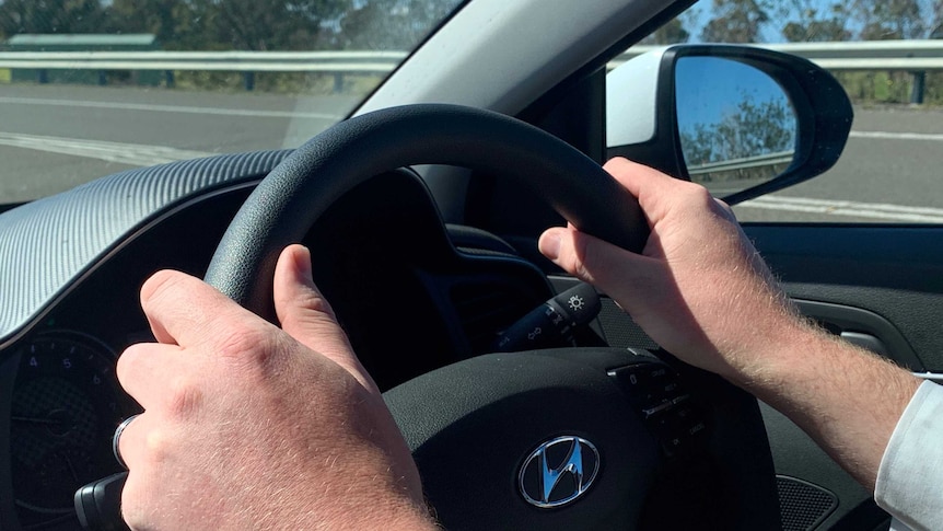 Closeup of a man's hands on the steering wheel of a car.