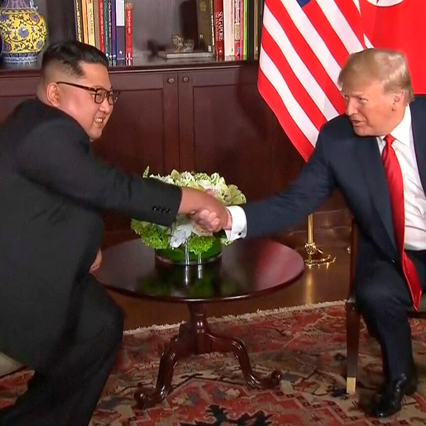 Donald Trump and Kim Jong-un sitting down, shaking hands in Singapore.