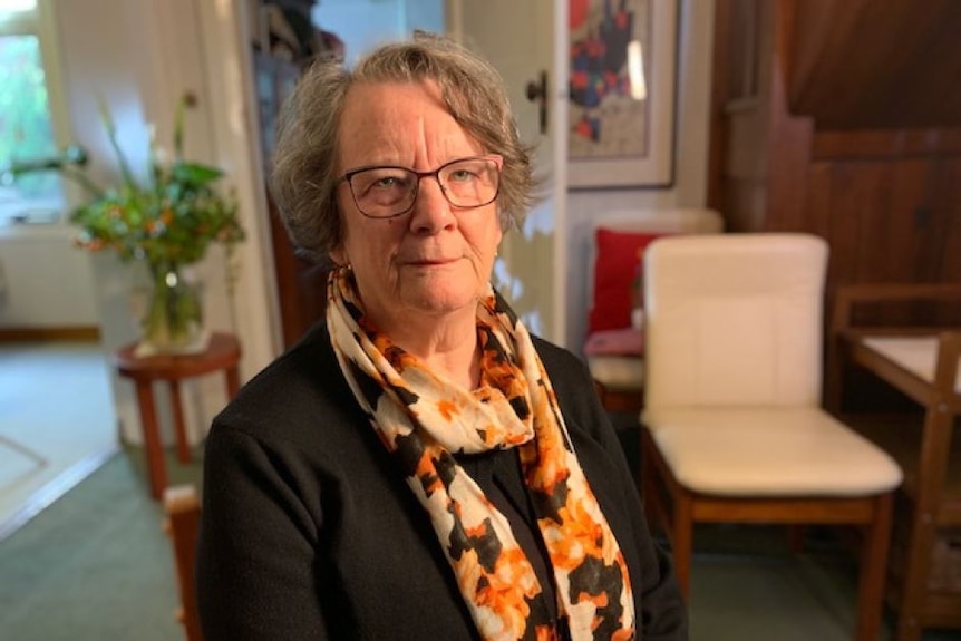 A woman wearing glasses and a scarf looks at the camera