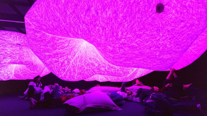 People nap under an illuminated art installation