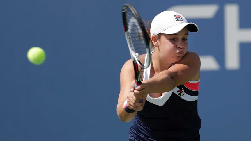 Tennis player Ashleigh Barty holds the racquet with two hands and swings at the ball.