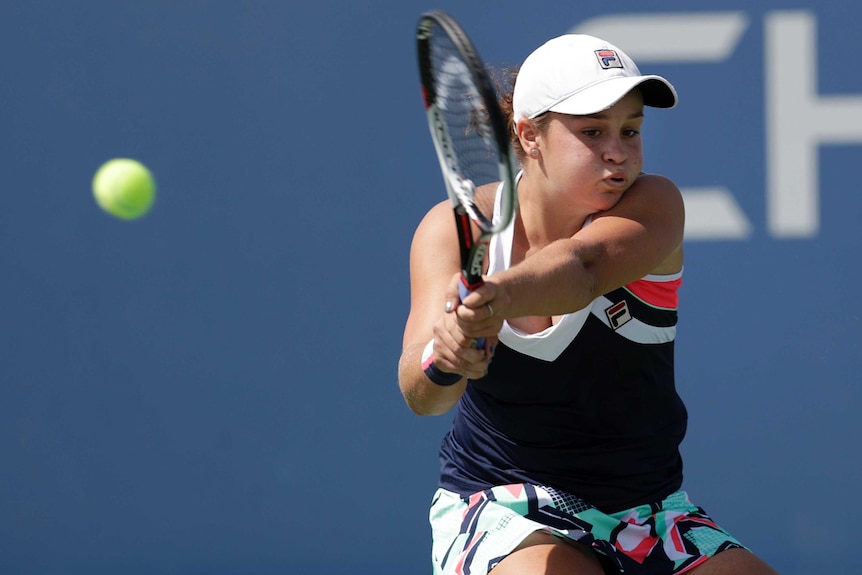 Tennis player Ashleigh Barty holds the racquet with two hands and swings at the ball.