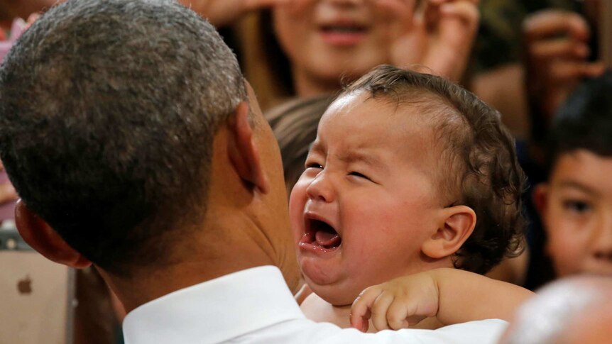 US President Barack Obama holds a crying baby.