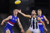 An AFL ruckman gets his hand to the ball to tap it clear while his opponent watches.