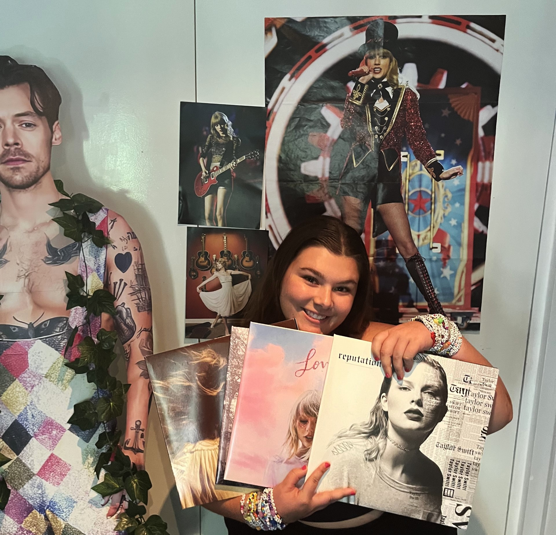 A woman smiles and holds up four Taylor Swift records in front of her.