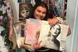 A woman smiles and holds up four Taylor Swift records in front of her.