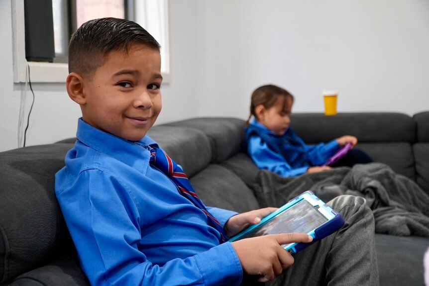 A little boy in a school uniform uses a ipad 