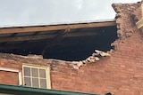 Several bricks missing from a wall, making a large hole in the side of a building.