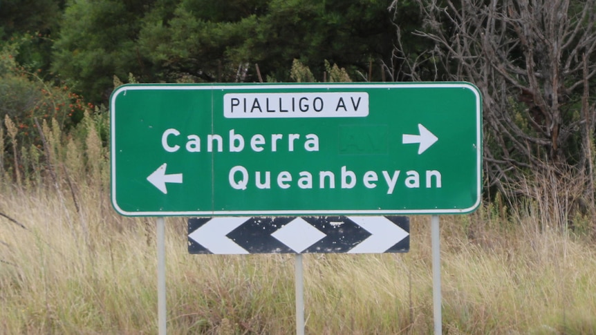 A roadside sign showing Queanbeyan is 4 kilometres in one direction and Canberra is 13 kilometres the other way.