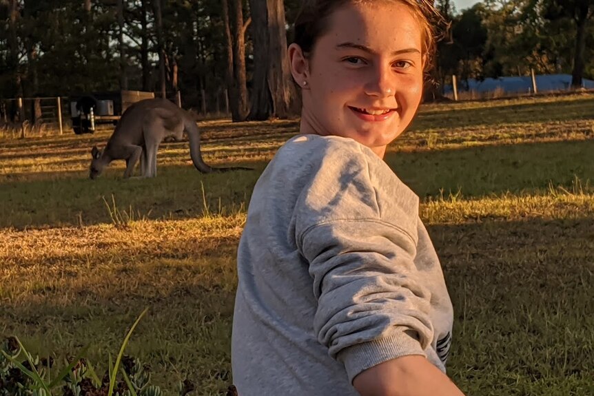 Mackenzie smiles in some bushland with a kangaroo.
