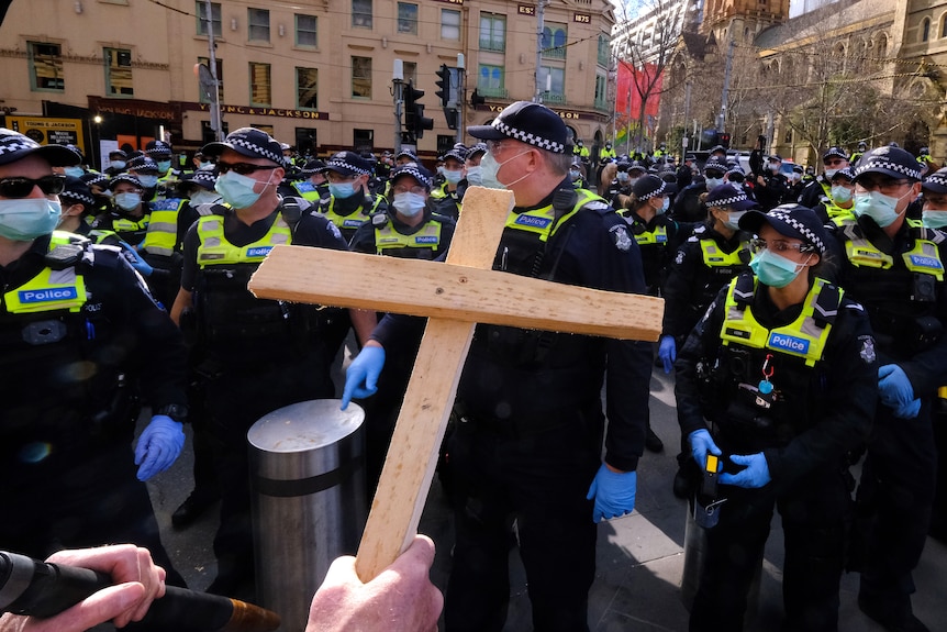 A protester holds a wooden cross in front of a group of police during a demonstration. 