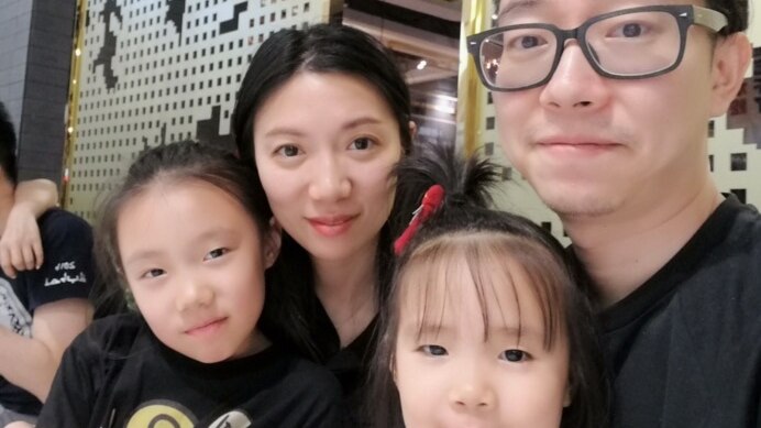 Lucy Ly sits next to her husband, who wears glasses. Two young children sit, one on each of their laps.