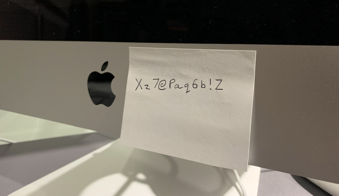 A post-it note stuck on a computer with a password written on it.