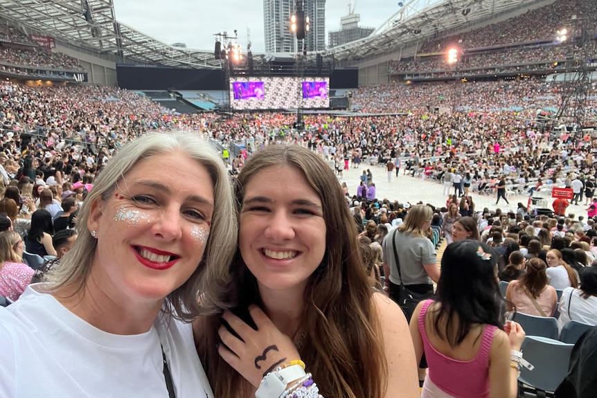 A mother and daughter pose for a photo in front of a crowd gathered for a Taylor Swift concert