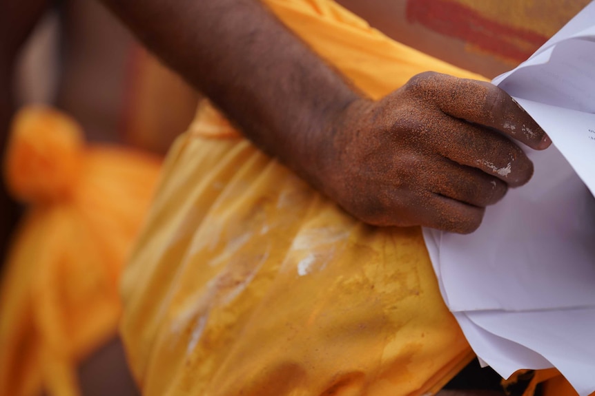 Michael's hand covered in red dirt holds his speech - flecks of paint are visible on his hand.