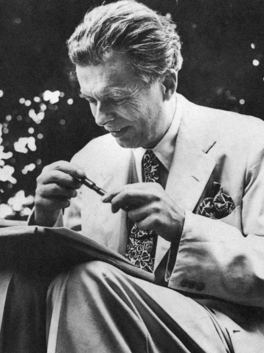 Aldous Huxley sits outdoors with a pen and paper