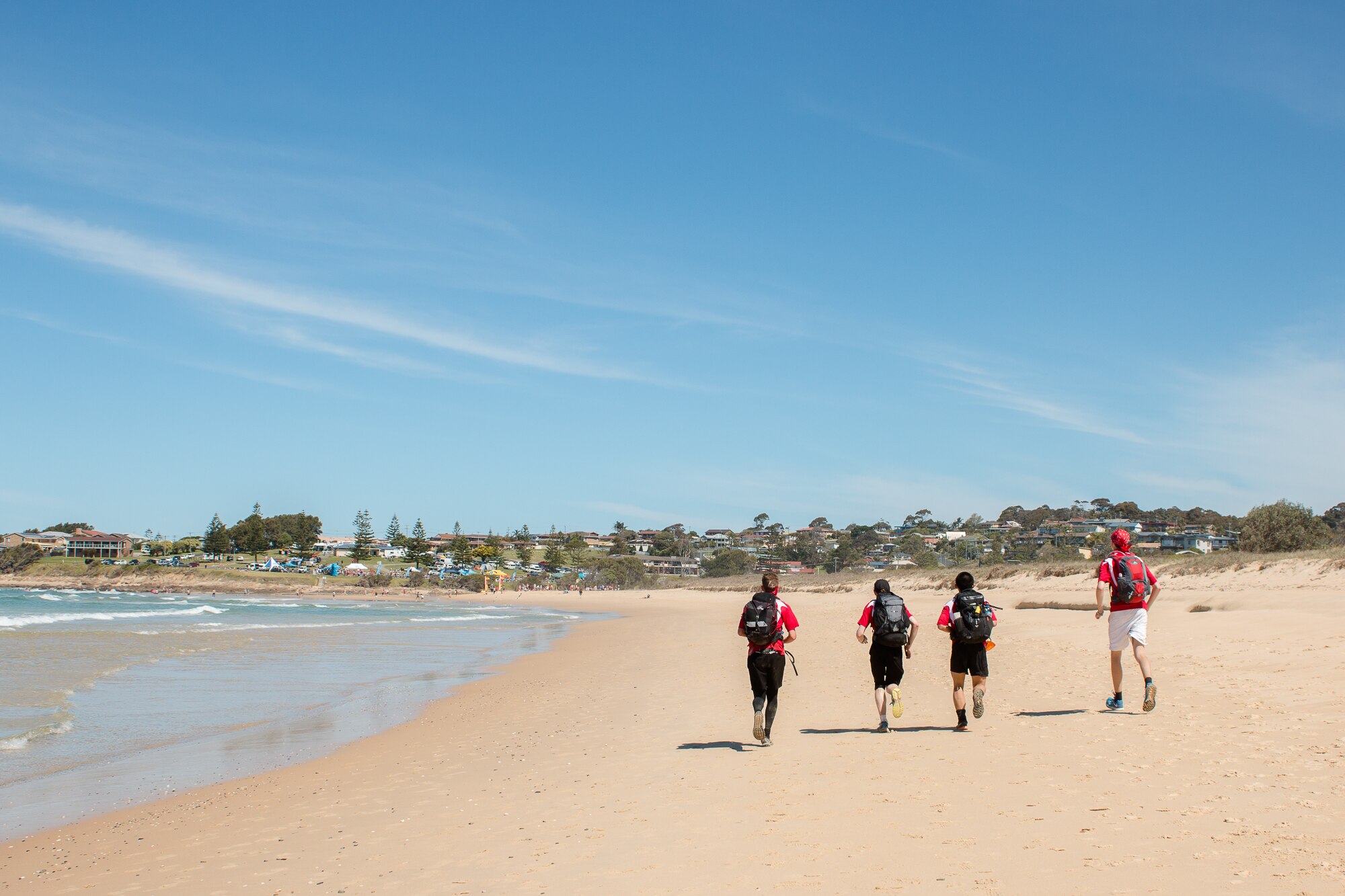 Four people in the distance run on the beach, with their backs towards the camera.