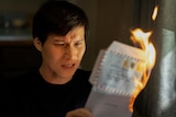 A film still of Hoa Xuande, a Vietnamese Australian man with a distressed expression, holding a burning letter.