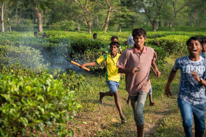 Kids and young men run through the tea fields. One boy is holding a firecracker.