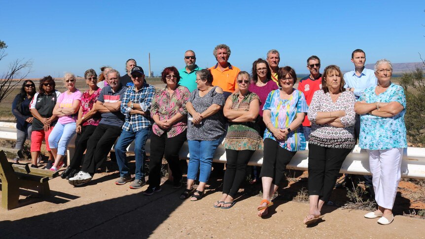 Twenty residents stand outside with the closed power station behind them