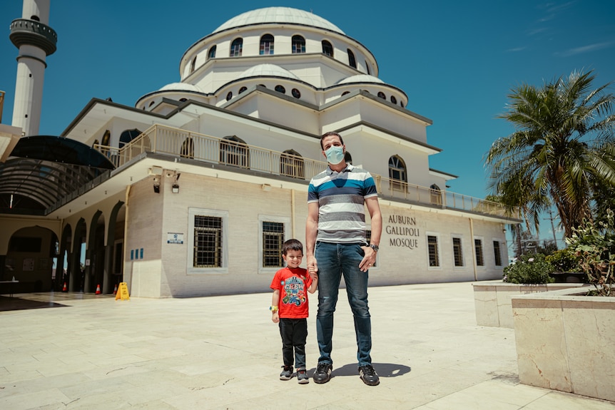 Man holding a small boy's outside standing outside a mosque. 