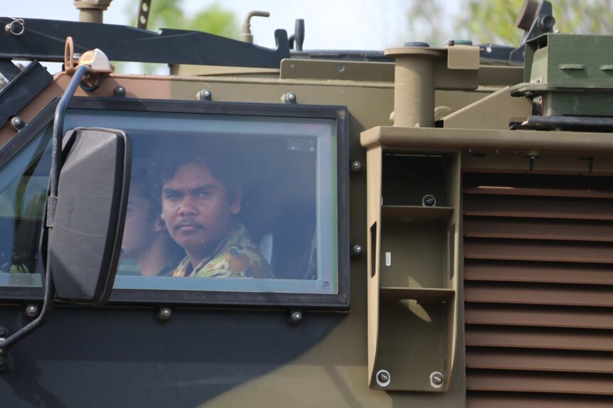 Two Indigenous teens ride in an army tank