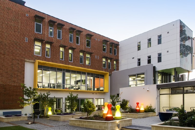 A wide shot of a four-storey brick and white residential building with a courtyard and gardens in front of it.