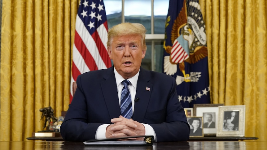 Donald Trump looks directly at the camera while sitting at his Oval Office desk