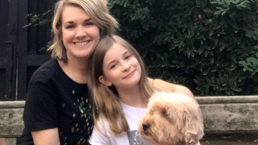 A woman and a child cuddle a dog in the garden