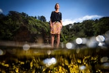 Michelle Voyer stands in a patterned skirt and black top by the water's edge with the tide out of focus in the foreground.