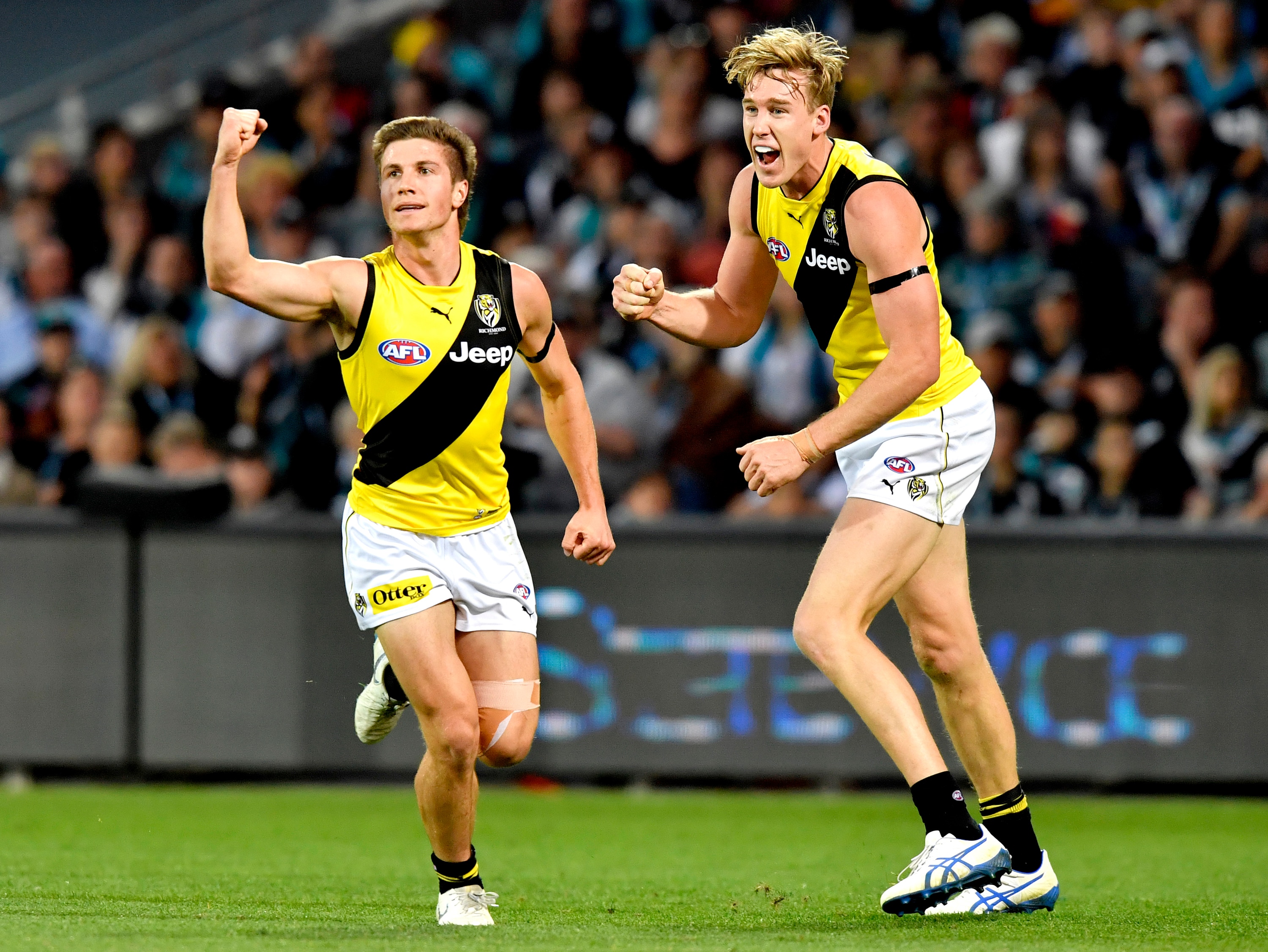 An AFL player pumps his fist in celebration while running ahead of a teammate