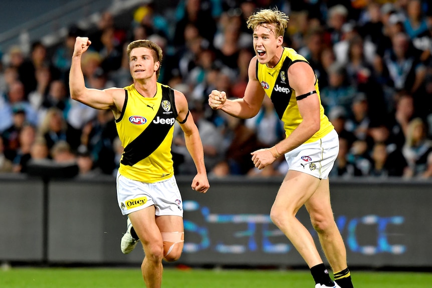 An AFL player pumps his fist in celebration while running ahead of a teammate