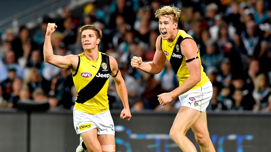 An AFL player pumps his fist in celebration while running ahead of a teammate