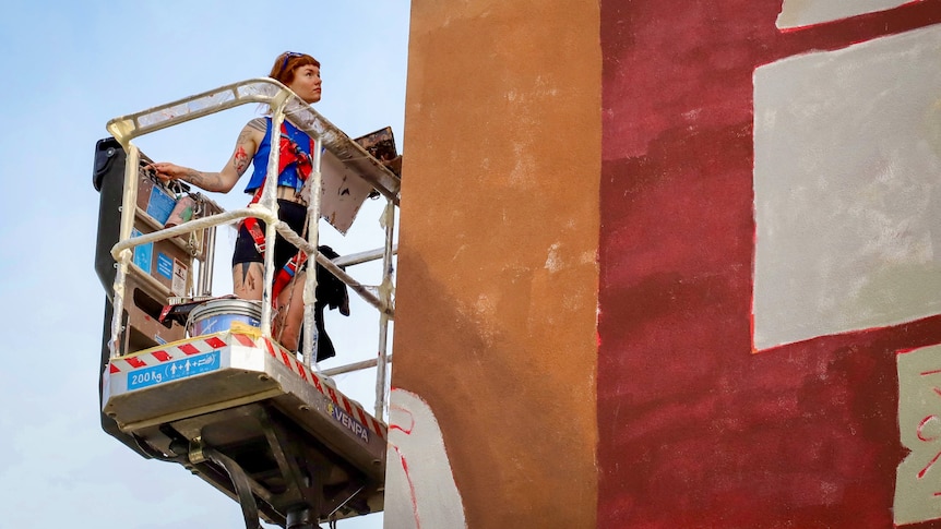 The artist up on a crane, examining the wall they are painting.