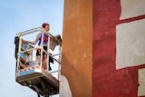 The artist up on a crane, examining the wall they are painting.