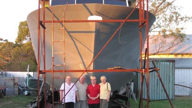 Henry Freise stands with 3 people in front of large boat in a backyard