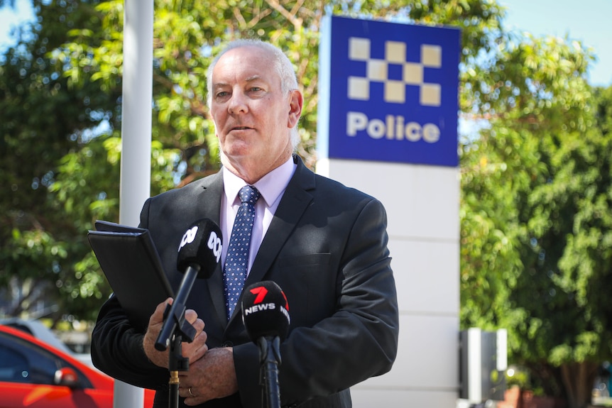 A male detective speaks at a press conference outside a police sign