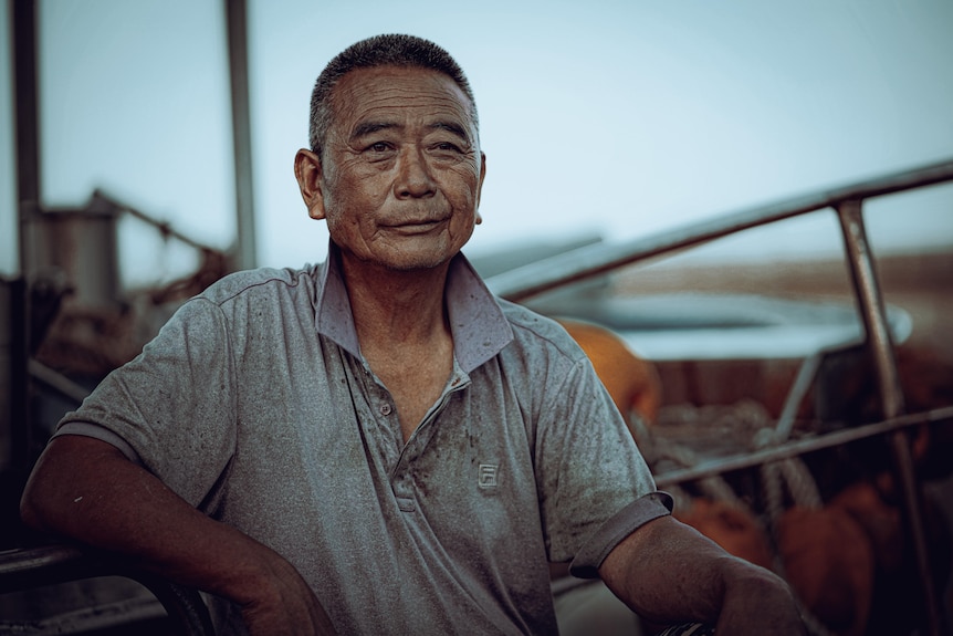 An older South Korean man looks out to sea from his boat with a slight smile on his face 