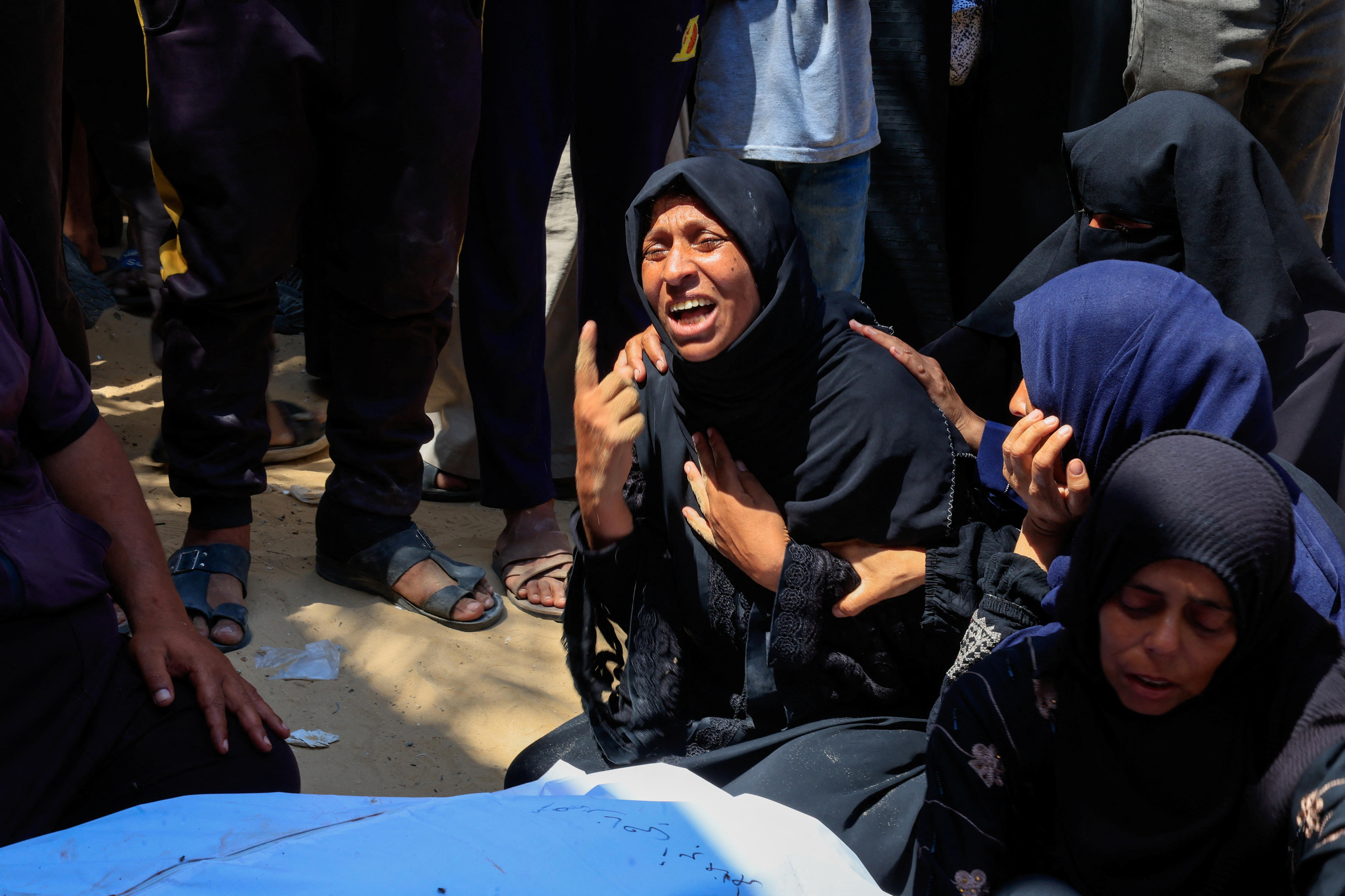 A woman crying on the ground in a crowd out the front of a hospital.
