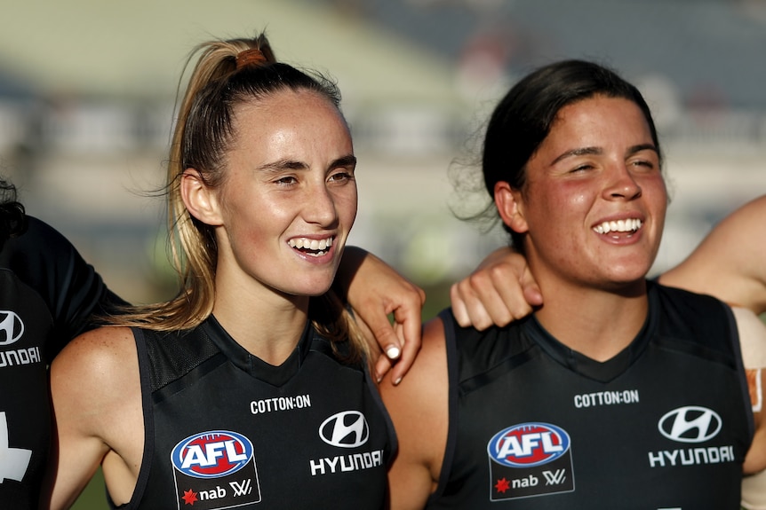 Georgia Gee and Maddy Prespakis stand arm in arm singing the Carlton theme song