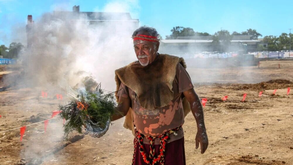 Indigenous male dressed in cultural attire conducting a traditional smoking ceremony in Townsville. 