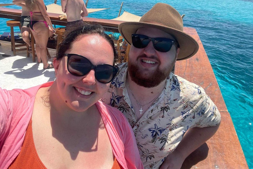 Lachie Dent and Chantelle Bongers smiling in a selfie taken at a bar next to bright blue water. 