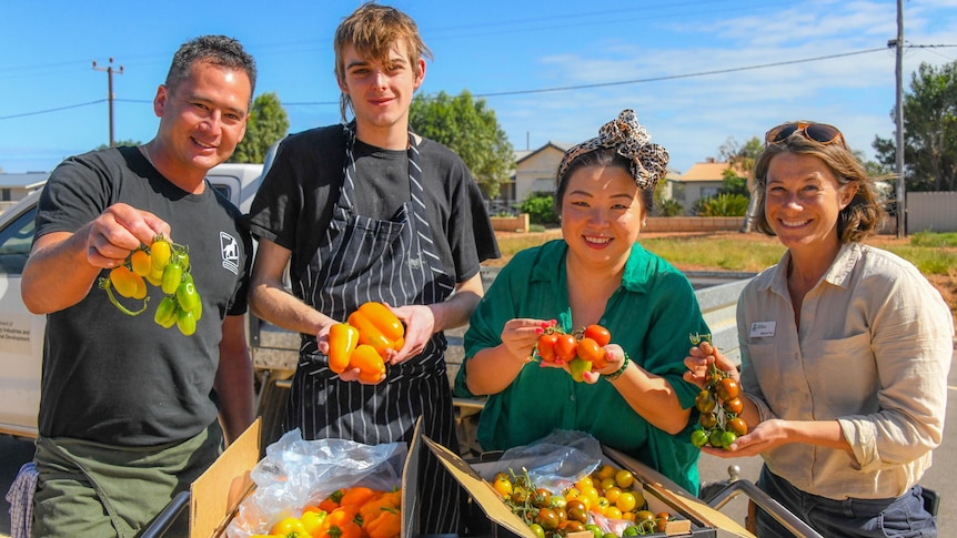 4 people holding fruit and vegetables smiling at the camera