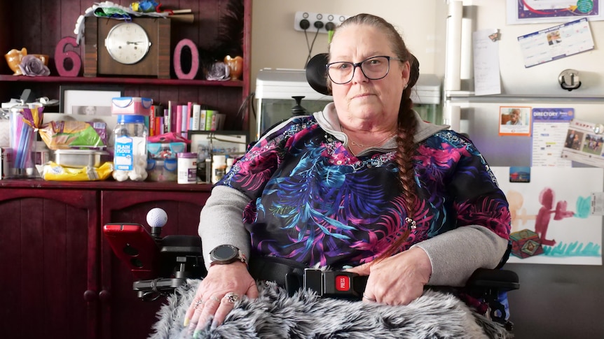 A middle-aged woman sits in her electric wheelchair inside her dining room. 