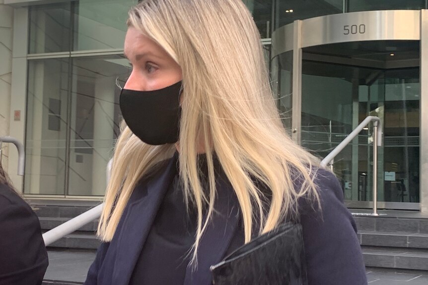 Un gros plan de Rachel Roche quittant le tribunal, vêtue d'un costume noir et d'un masque COVID.