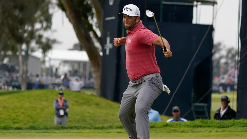 Jon Rahm punches the air while holding his putter at the US Open golf.